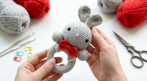 Kyle Coelho Amigurumi em algodão macio bege com detalhes em cores suaves, ideal como chocalho artesanal para bebês.