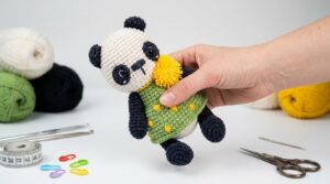 Panda Amigurumi Pequeno com detalhes em preto e bege em crochê, posicionado para exibição decorativa em artesanato.