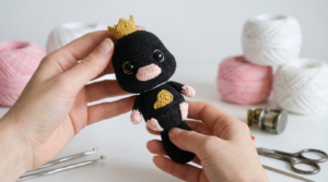 Patrón de Pelúcio amigurumi tejido en hilo de algodón azul marino con texturas suaves y detalles en rosa para accesorios decorativos de ganchillo.