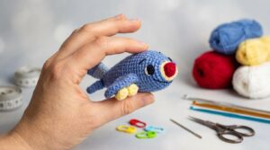Aviao de croche amigurumi azul com detalhes coloridos, peça artesanal feita a mao exibida para decoracao infantil.