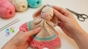 naninha de coelho amigurumi receita gratis passo a passo, peça artesanal de crochê bege com detalhes em rosa e azul para bebês.