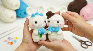 Par de coelhos de crochê amigurumi em tons pastéis delicados, exibindo detalhes artesanais para decoração de quartos infantis.